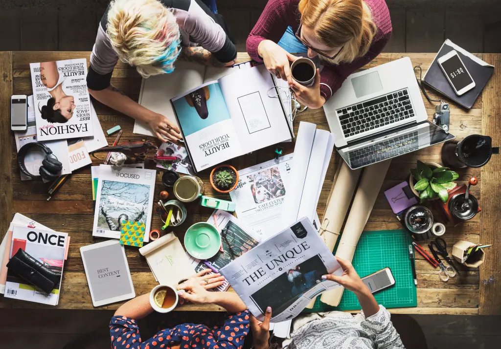 Équipe réunie autour d’une table avec un ordinateur, des magazines et du matériel photo